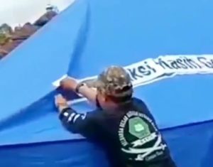 sejumlah warga sedang mencopot tulisan Tim Aksi Kasih Gereja Reformed Injili Indonesia yang ditempel di tenda warna biru yang ada di lokasi pengungsian korban gempa Cianjur.