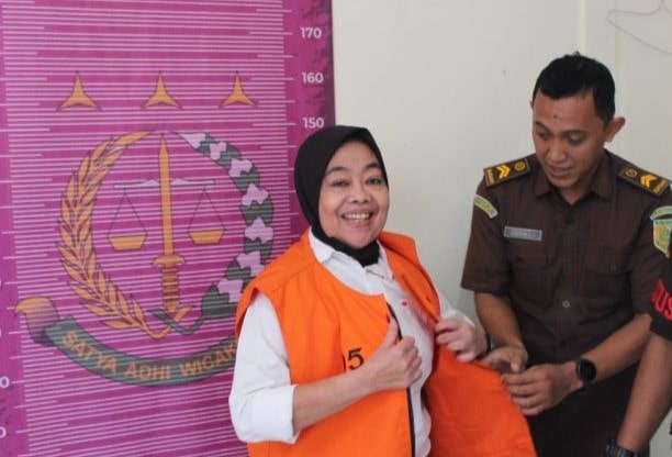 Meski telah menyandang status tersangka, mantan Kepala Desa (Kades) Cikujang, Kecamatan Gunungguruh, Kabupaten Sukabumi, berinisial Heni, tetap menebar senyum saat digiring ke Kantor Kejaksaan Negeri (Kejari) Sukabumi pada Senin, 28 Juli 2025. Dengan mengenakan rompi oranye khas tahanan, Heni tampak tenang meski kini harus mempertanggungjawabkan dugaan penyalahgunaan dana desa.